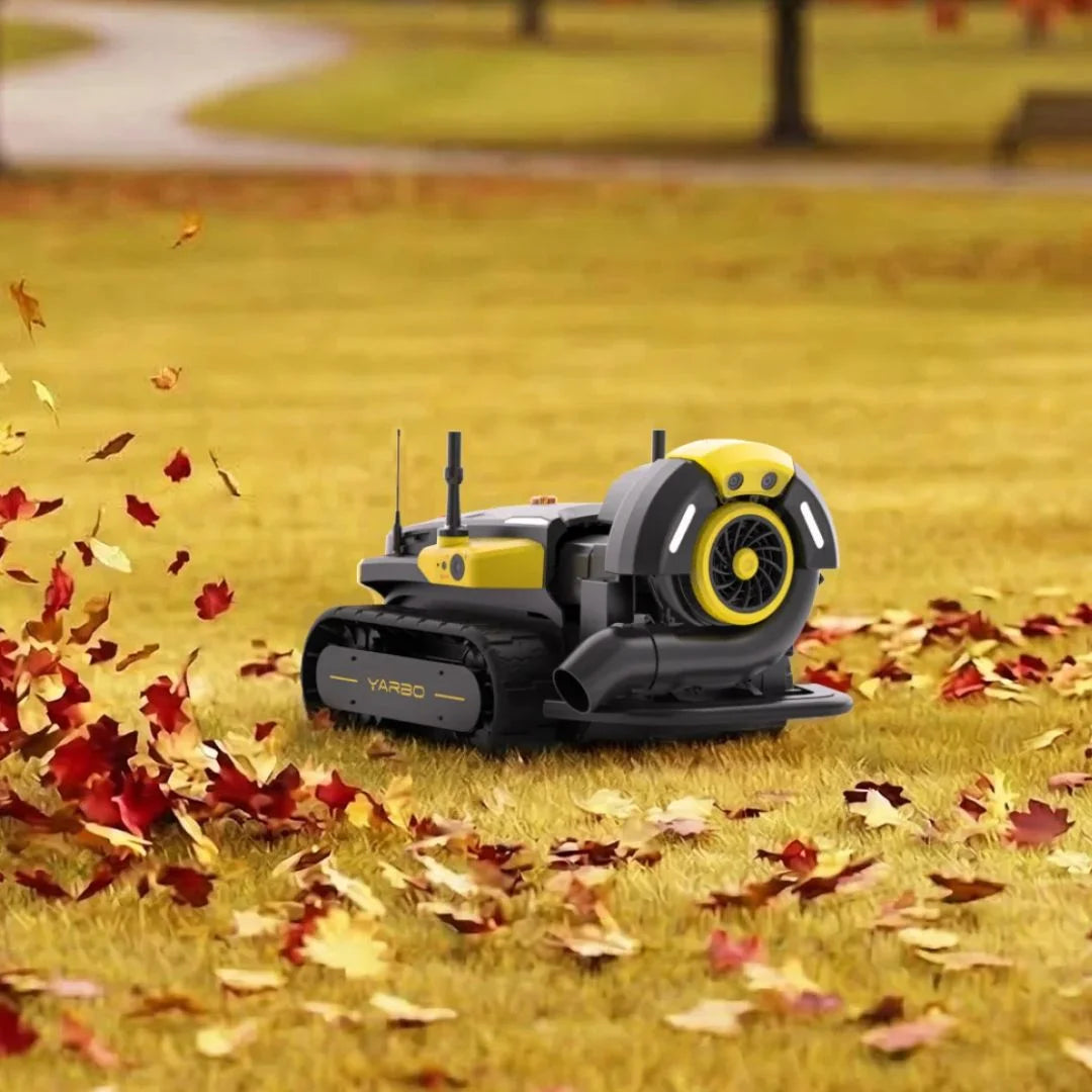 A yellow and black tracked robotic leaf blower is shown outdoors on a grassy lawn with scattered red and yellow autumn leaves. The robot has visible branding that reads VARBO on the side.