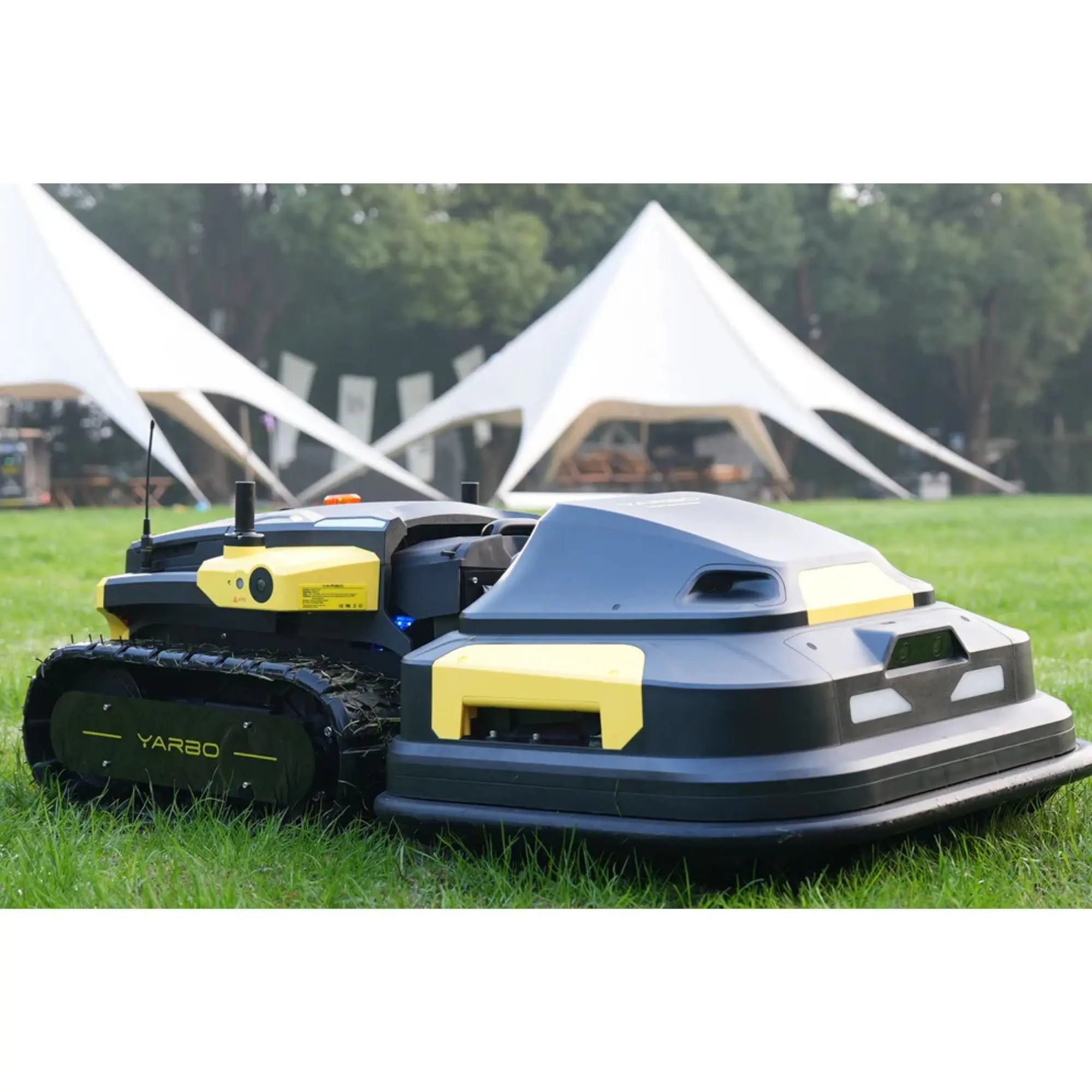Robotic lawn mower on grass with tents in the background