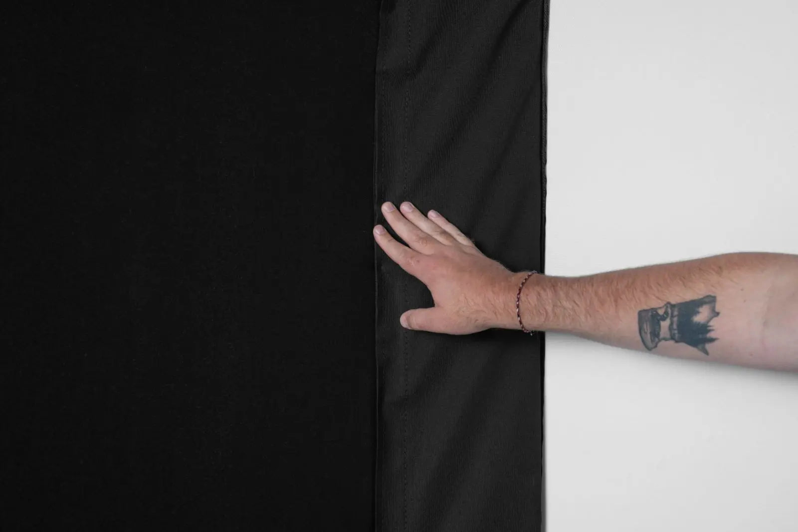 Person's arm with a tattoo holding a black panel between a dark and light background